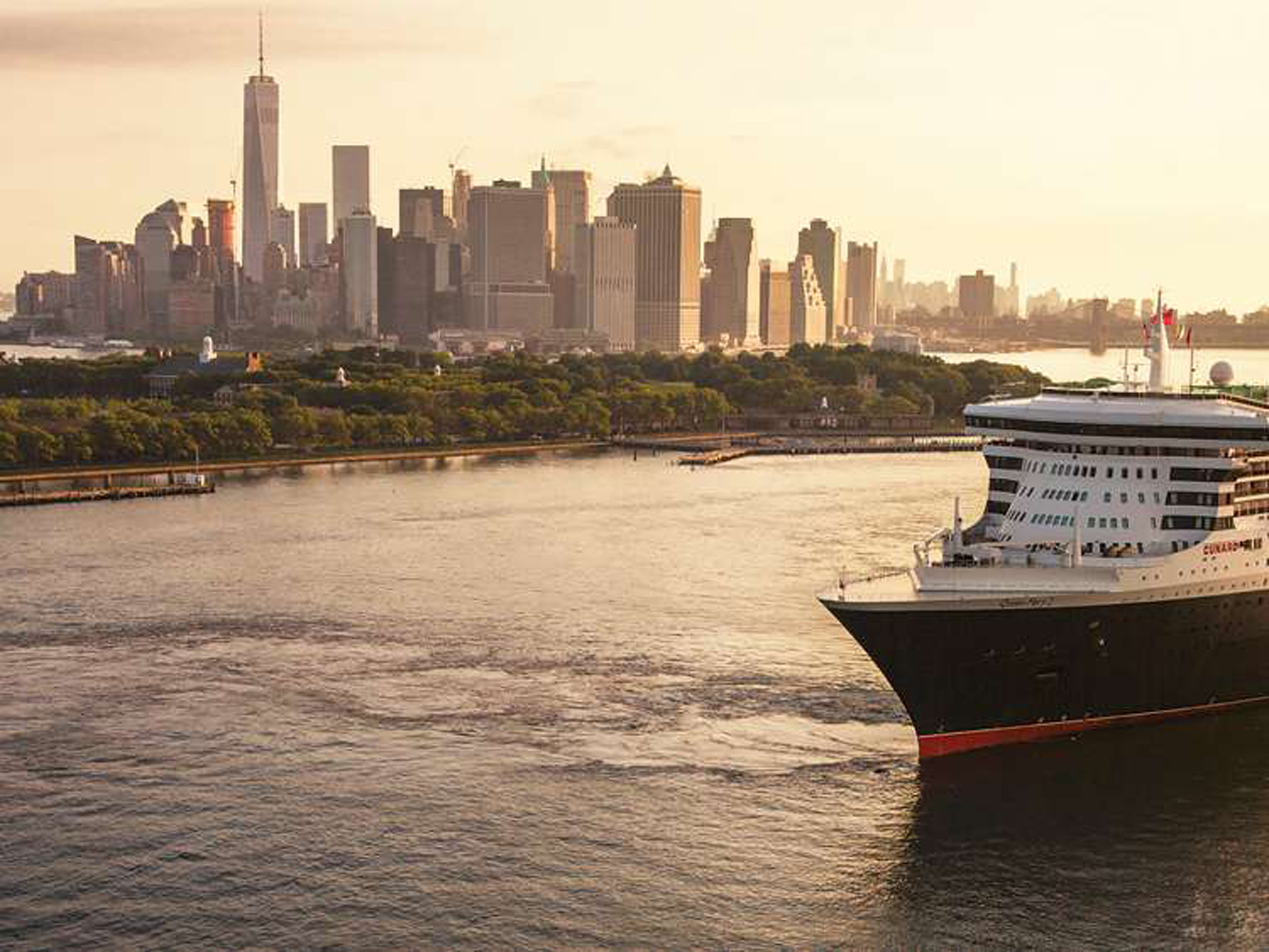 A majestic ocean liner docked in New York Harbor with the iconic Manhattan skyline bathed in golden hour sunlight. The ship's distinctive black hull and white superstructure contrast beautifully against the towering skyscrapers and lush waterfront greenery of lower Manhattan.