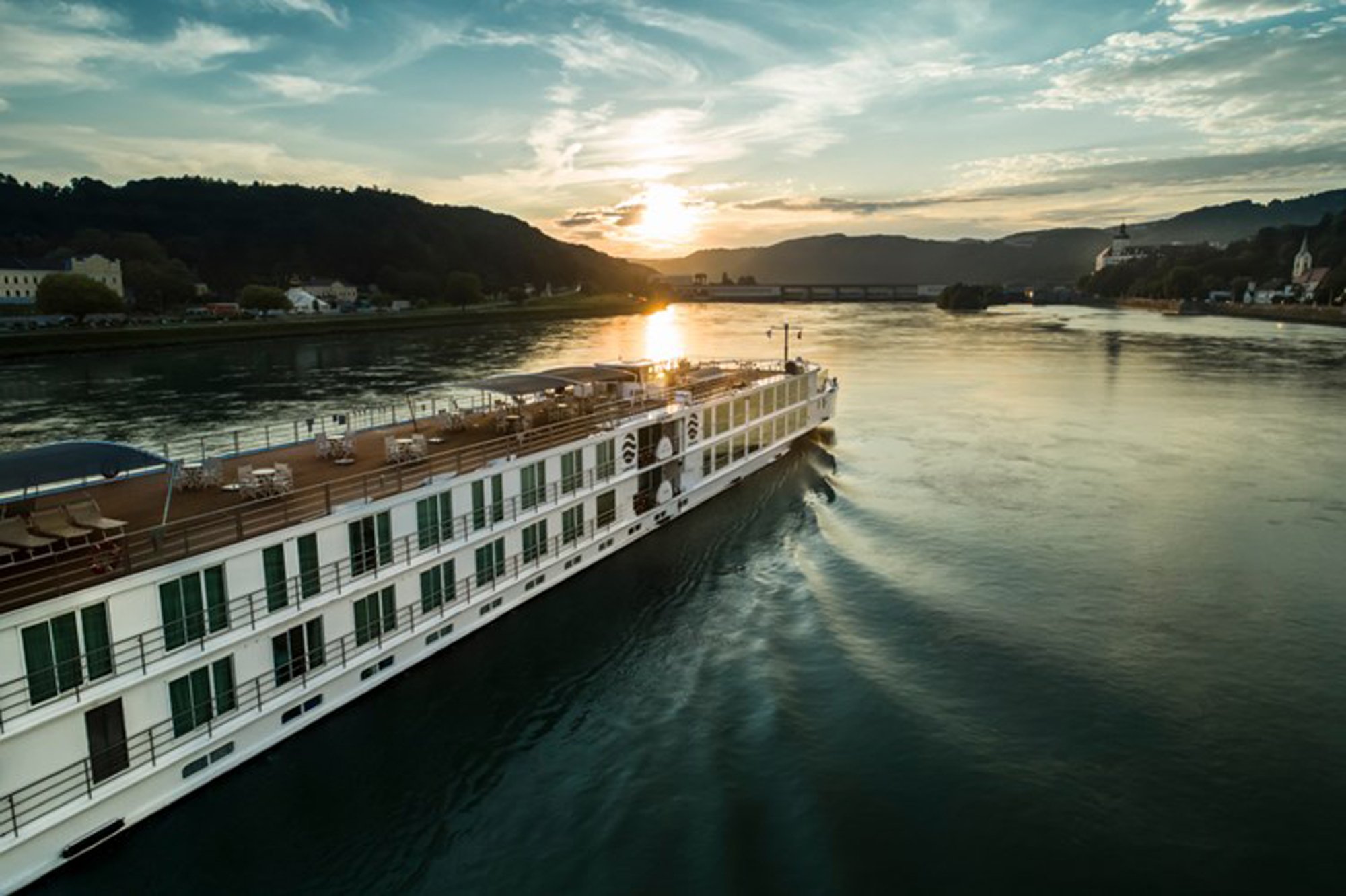 2224_50034_resize_0_500 River cruise ship at sunset navigating a scenic alpine valley with forested mountains and charming riverside villages