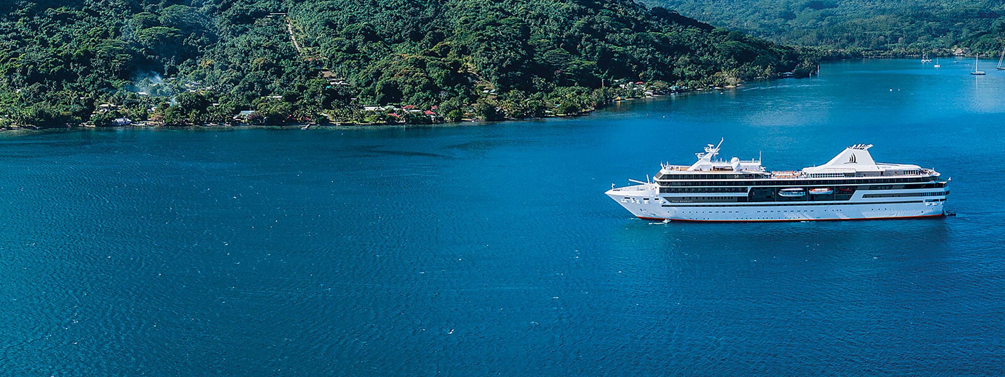 Luxury cruise ship anchored in crystalline turquoise waters alongside a lush tropical coastline in French Polynesia