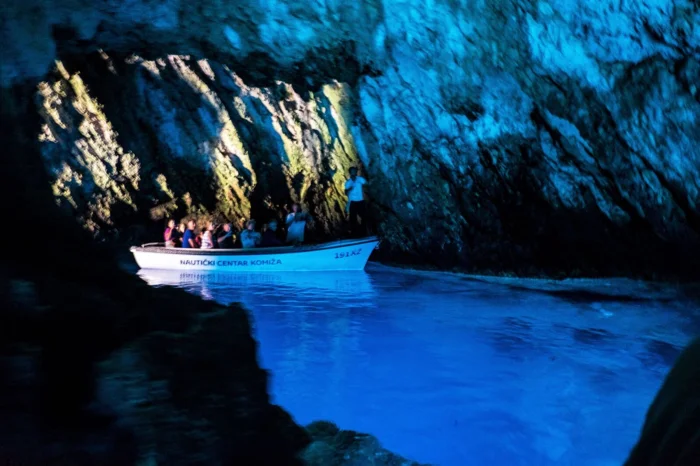 Blue Grotto Cave Boat Tour A small tour boat filled with passengers navigates through a stunning sea cave illuminated by brilliant blue water and golden limestone formations.
