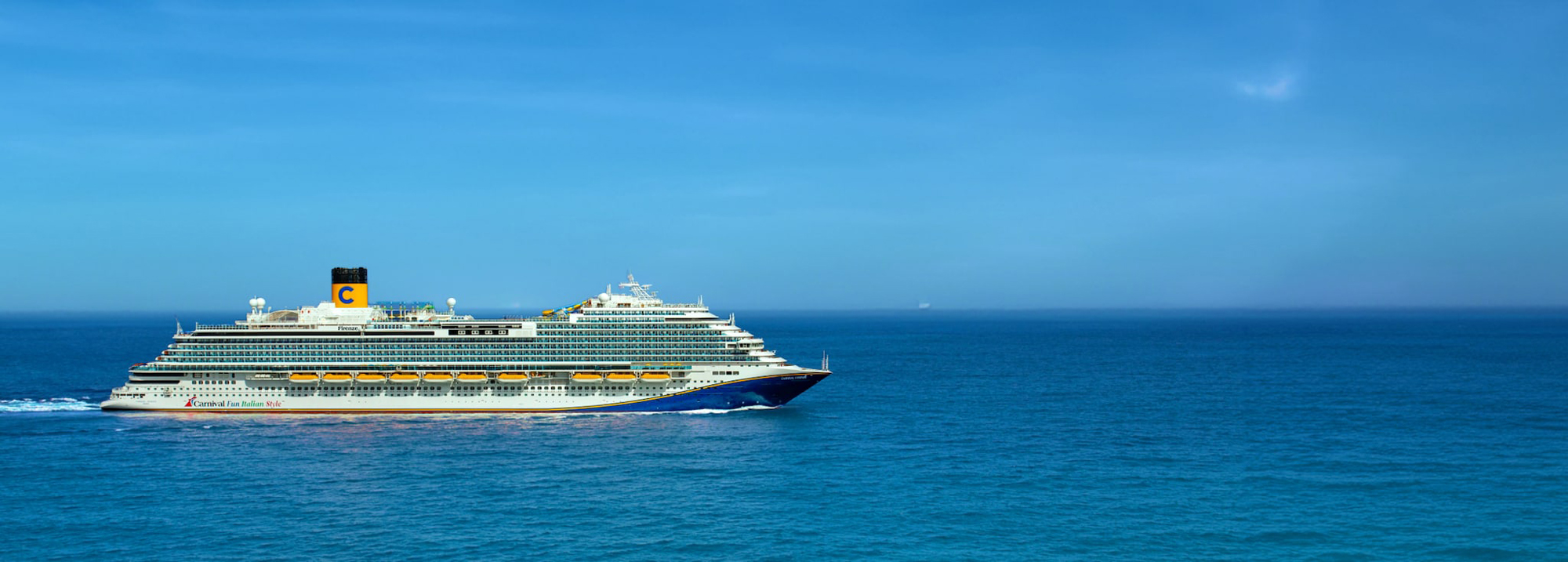 Carnival Cruise Ship on Blue Ocean A large Carnival cruise ship sailing on a calm, vibrant blue ocean under a clear sky. The vessel