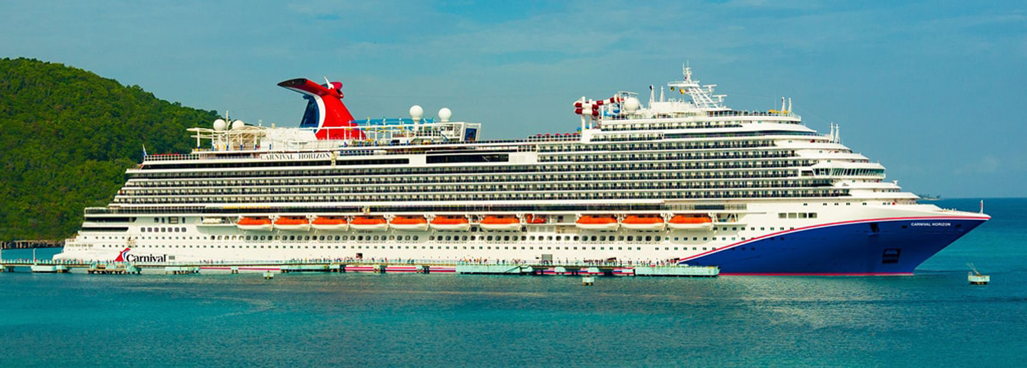 Carnival Horizon Cruise Ship in Tropical Port A large white and blue Carnival cruise ship docked in a turquoise bay with lush green mountainous