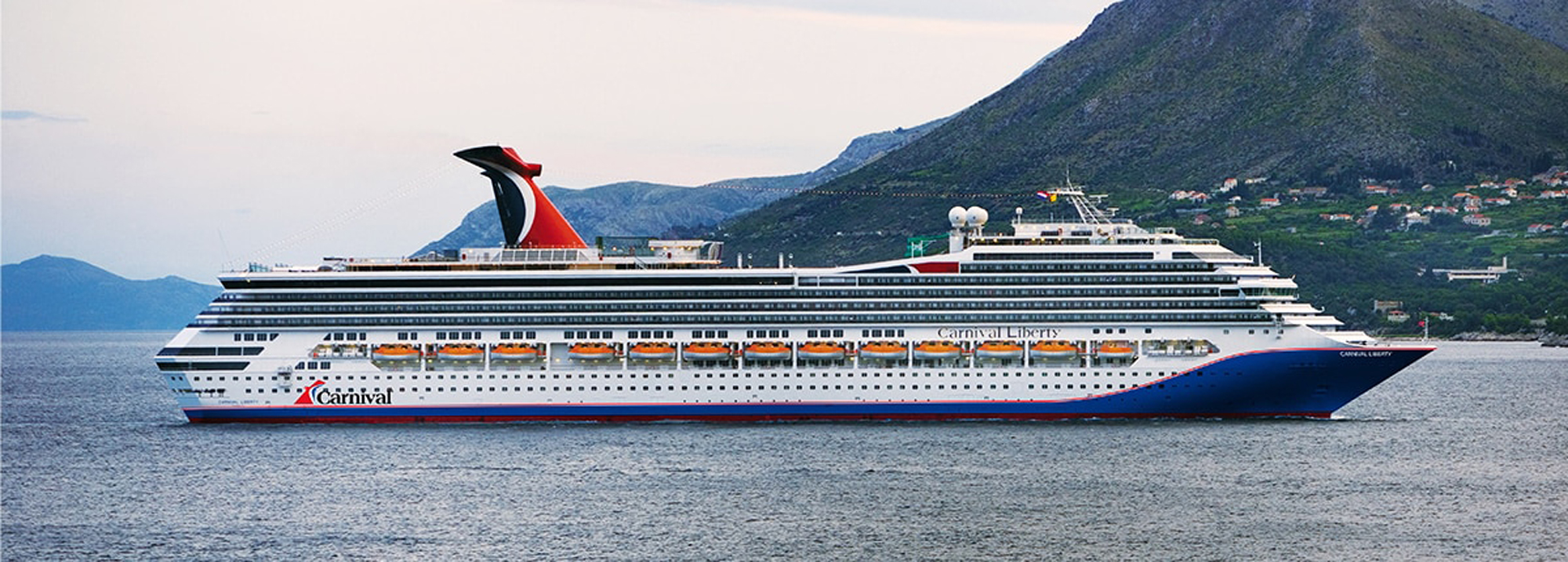 Carnival Liberty Cruise Ship in Mountain Landscape A large Carnival cruise ship sailing near a mountainous coastline with green hills and buildings