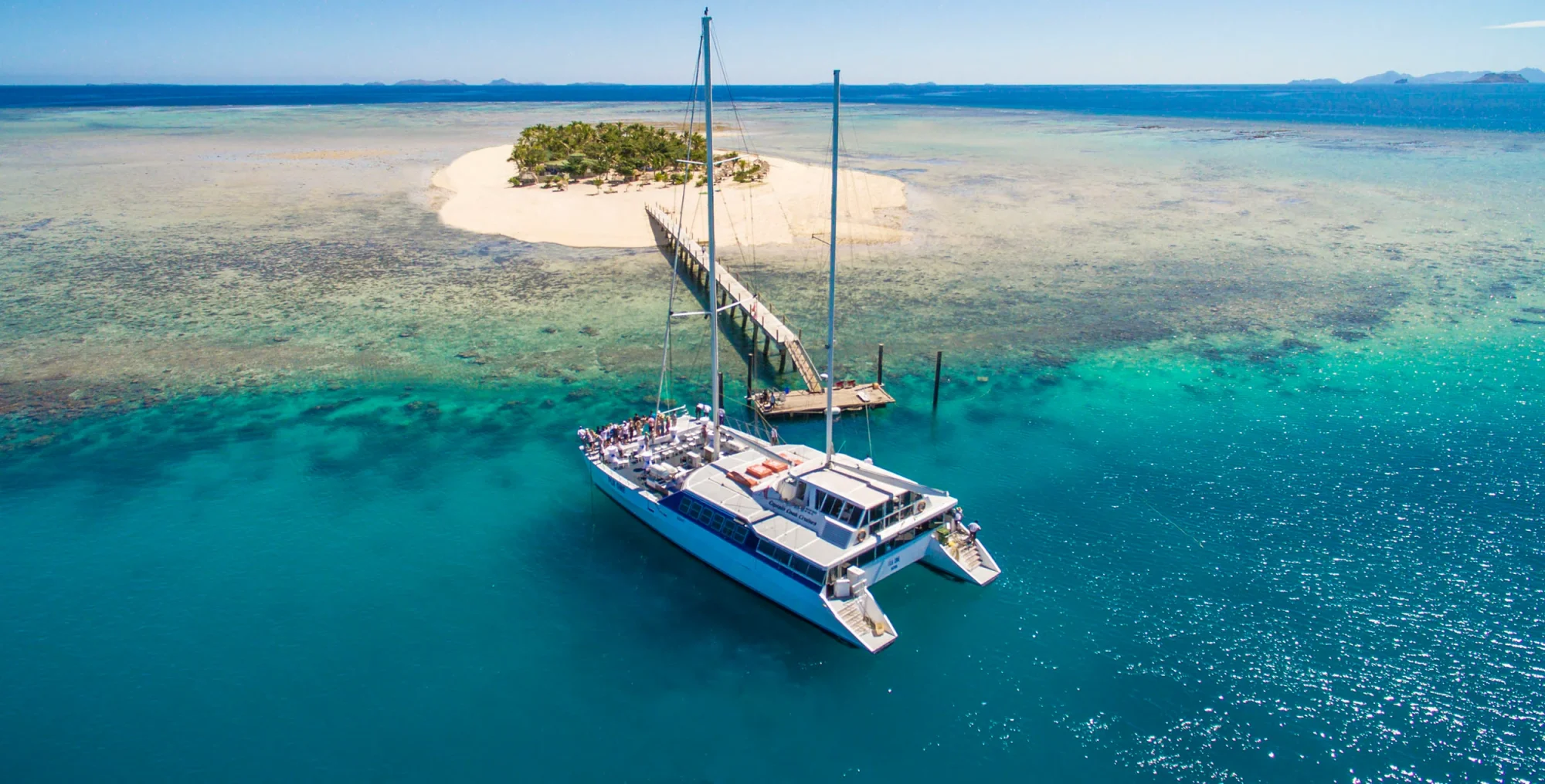 Catamaran at Tropical Island Paradise A blue and white catamaran anchors in crystal-clear turquoise waters near a pristine white sand