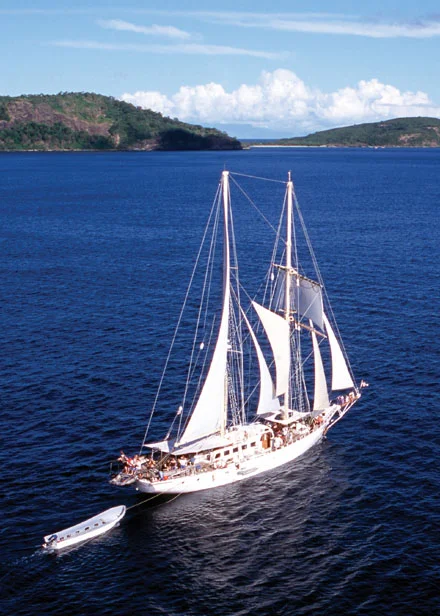 Classic Sailing Ship in Tropical Waters A stunning white-sailed tall ship glides through deep blue tropical waters with lush, forested
