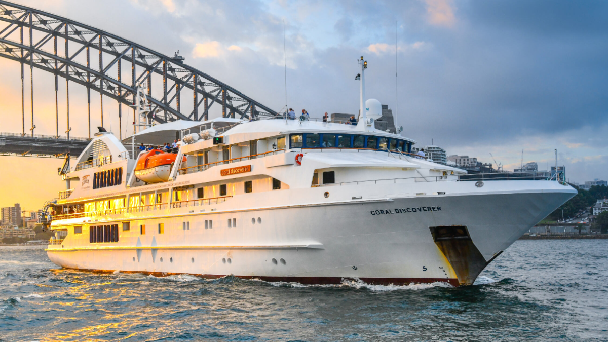 Coral Discoverer in Sydney Harbour A white expedition cruise ship named Coral Discoverer navigating through Sydney Harbour with the iconic Harbour Bridge in the background during golden hour lighting.