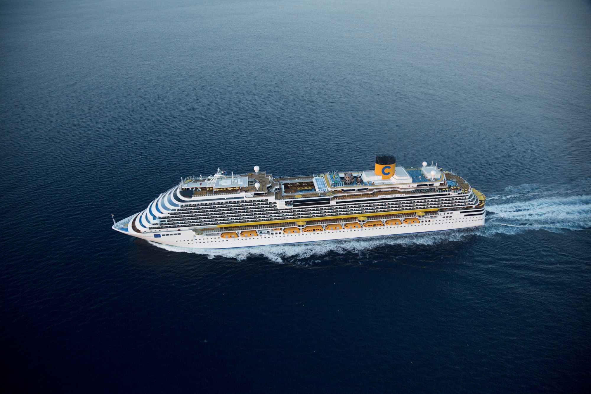 Costa Cruise Ship Sailing Blue Waters A large white and yellow Costa cruise ship sailing across a calm, deep blue ocean, showcasing the vessel's sleek design and impressive size.