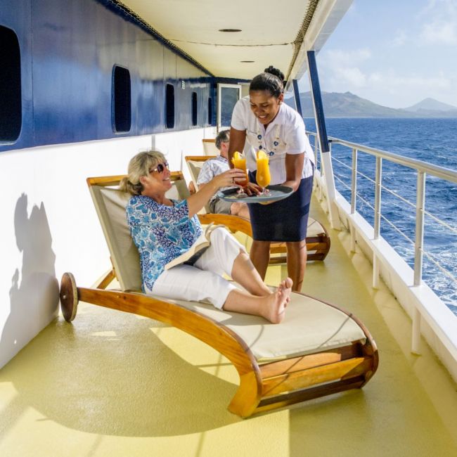 Cruise Ship Deck Service with Ocean View A crew member serves refreshments to a passenger relaxing on a lounge chair on the promenade deck
