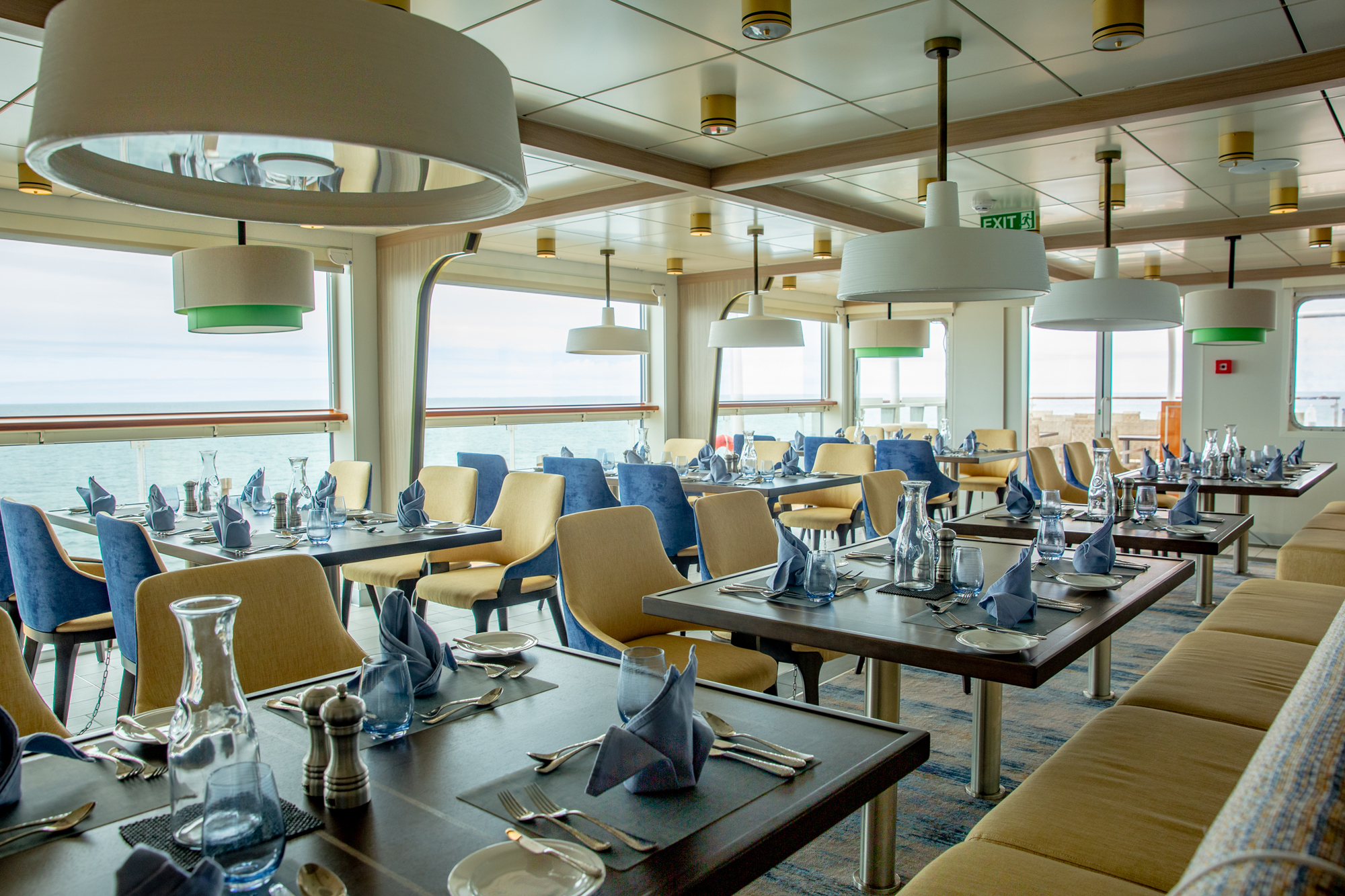Cruise Ship Dining Room with Ocean View Cruise ship dining room with ocean view through large windows, elegant table settings and modern decor.