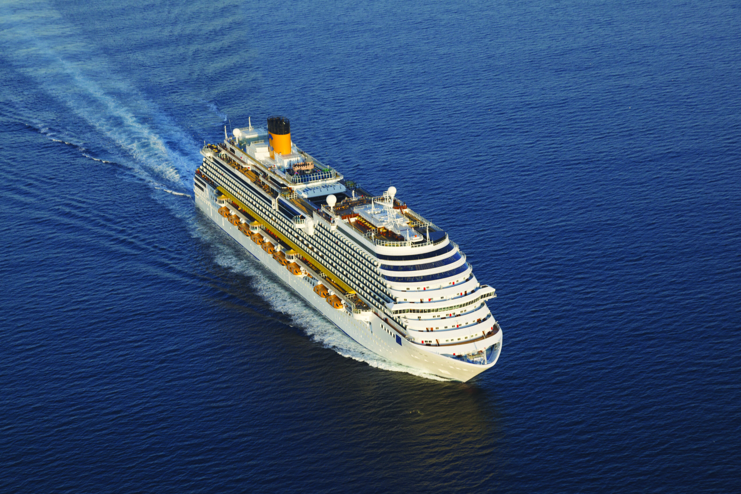 Cruise Ship Sailing Blue Open Waters A large white and yellow cruise ship sailing across a deep blue ocean, creating a distinctive wake