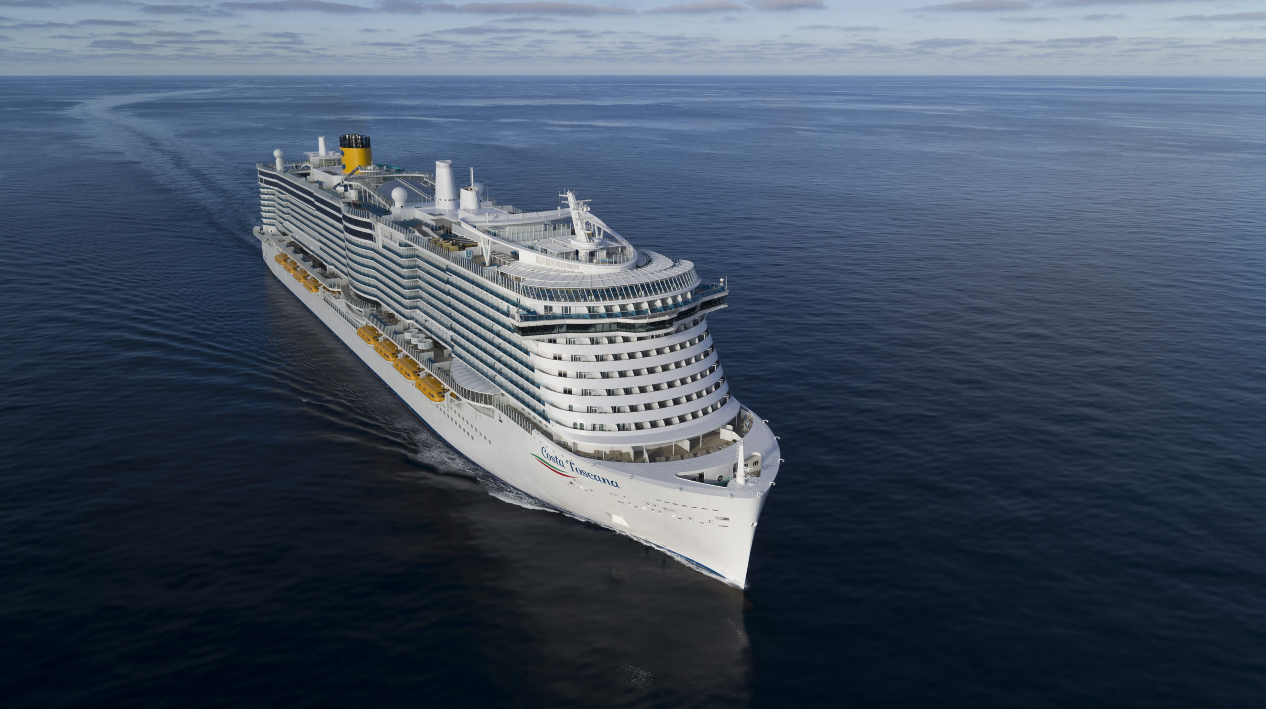 Cruise Ship Sailing on Calm Blue Ocean A large white cruise ship with yellow and white color scheme sailing across a serene, flat blue ocean under an overcast sky.