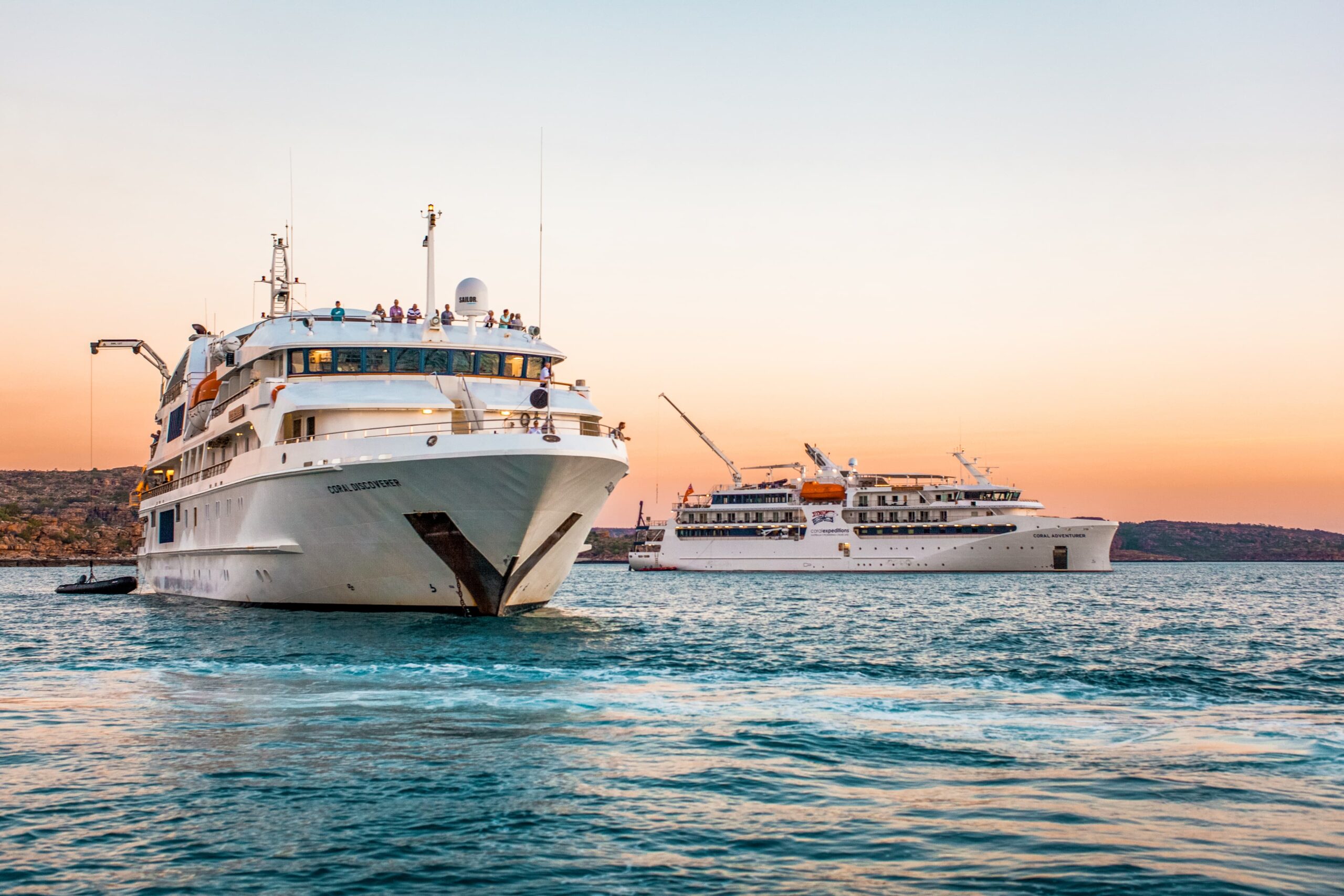 Cruise Ships at Sunset in Calm Waters Two white luxury cruise ships anchored in tranquil blue waters during a golden sunset, with rocky