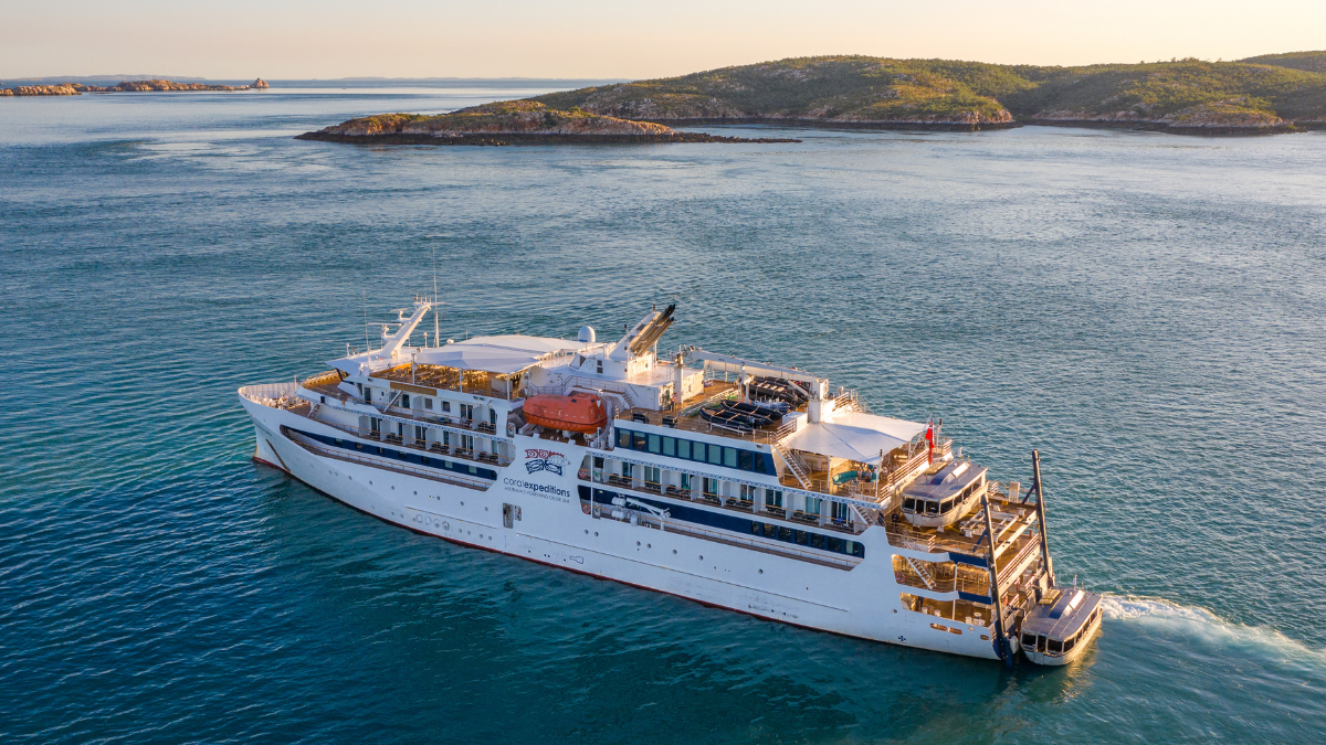 Expedition Cruise Ship in Coastal Waters A white expedition-style cruise ship navigating through blue waters near rocky coastal islands during golden hour lighting. The vessel appears to be a smaller, specialized cruise ship designed for adventure travel.
