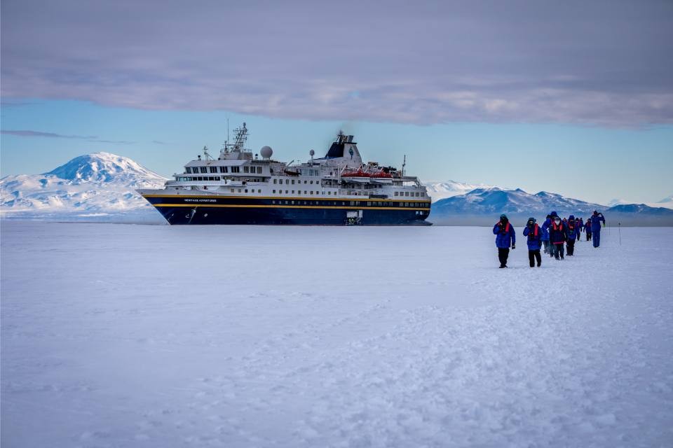 Expedition Ship at Antarctic Ice A large expedition cruise ship anchored in Antarctic waters with passengers walking across