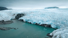 Glacial Lagoon with Turquoise Waters A stunning Arctic glacier descends steeply to meet turquoise glacial meltwater, with ice cliffs towering above rocky shores and mountains visible in the misty background.