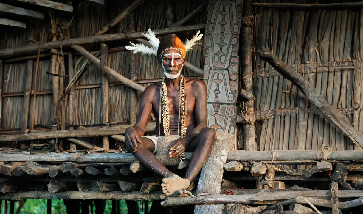 Indigenous Papua New Guinea Tribal Elder A dignified tribal elder from Papua New Guinea sits on a traditional wooden structure, displaying