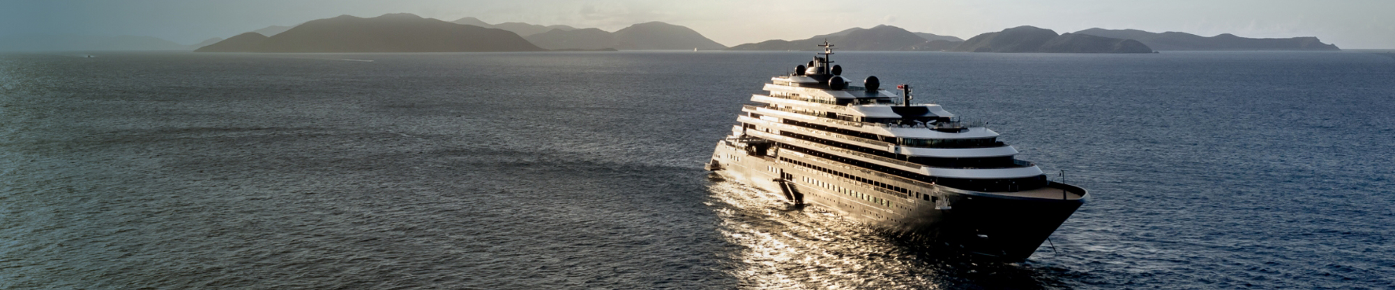 Luxurious Superyacht at Scenic Mountain Coast A sleek luxury yacht sailing on calm blue waters with a mountainous coastline in the background.