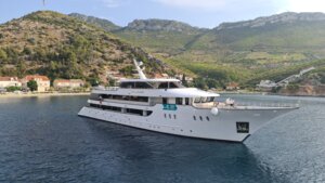 Luxury Cruise Ship Anchored in Mediterranean Bay A modern expedition-style cruise ship is anchored in calm turquoise waters near a picturesque