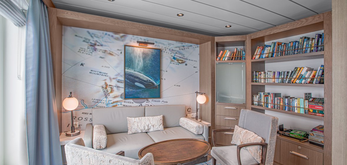 A contemporary cruise ship cabin featuring elegant bedding with neutral tones and modern furnishings typical of premium cruise line accommodations.