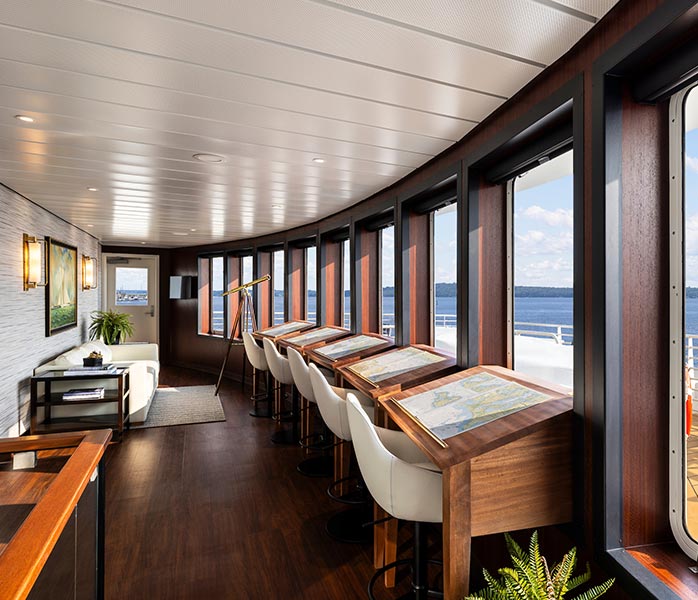 Luxury Cruise Ship Observation Lounge with Ocean Views An elegant observation lounge aboard a cruise ship featuring floor-to-ceiling windows overlooking the ocean, with contemporary furnishings including wooden accents, cream-colored chairs, and a sophisticated interior design combining dark wood flooring with white ceiling panels and warm lighting.
