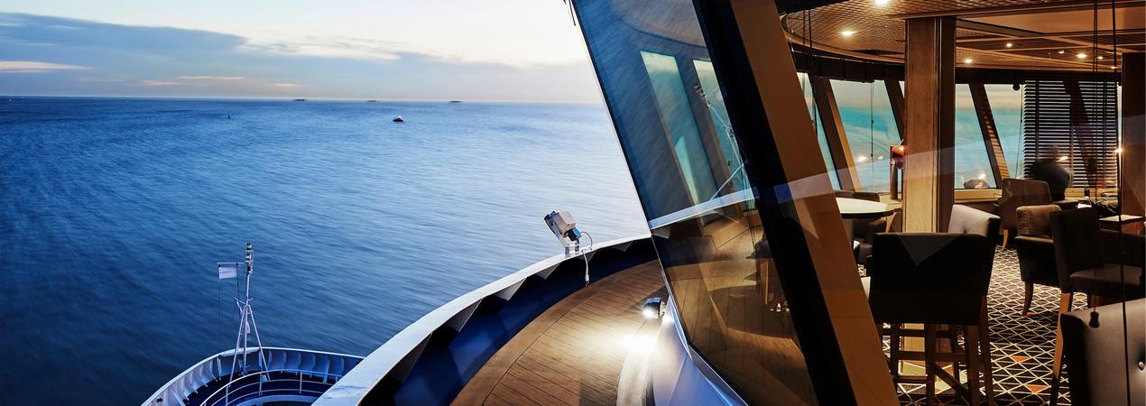 A panoramic view from a modern cruise ship observation deck, showcasing expansive blue ocean waters and an elegant interior lounge with large glass windows.