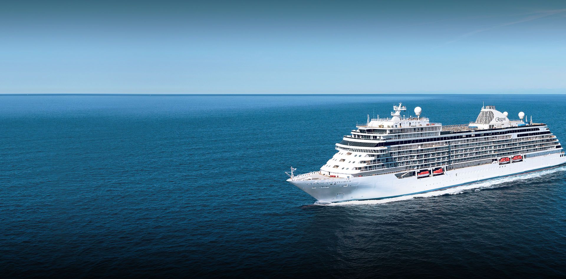 Luxury Cruise Ship Sailing Blue Ocean A pristine white luxury cruise ship sailing across a tranquil, deep blue ocean under a clear blue sky. The vessel appears to be moving at speed, creating a white wake against the calm sea.