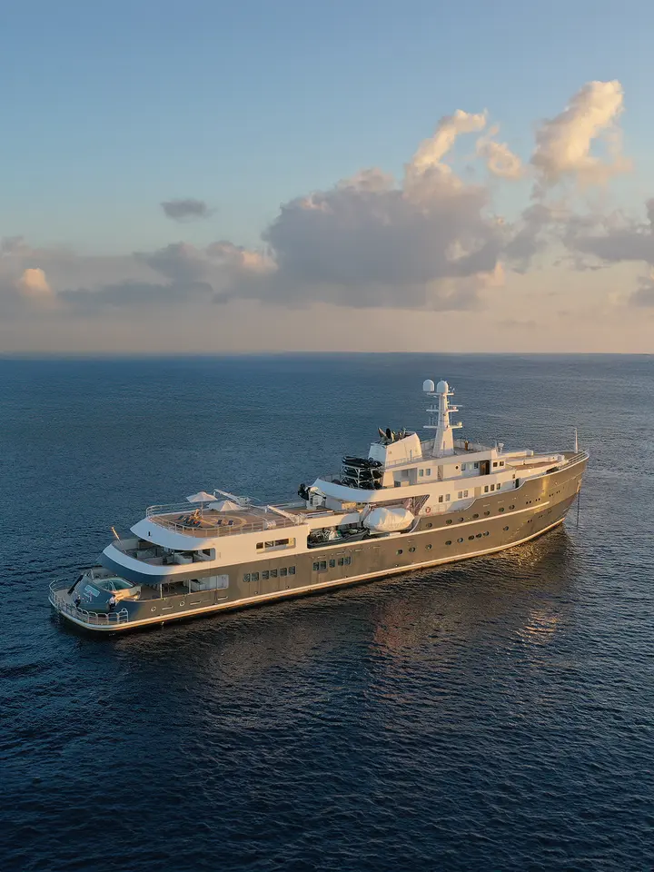 Luxury Expedition Yacht in Open Ocean A stunning golden-hulled expedition yacht anchored in calm blue waters during golden hour