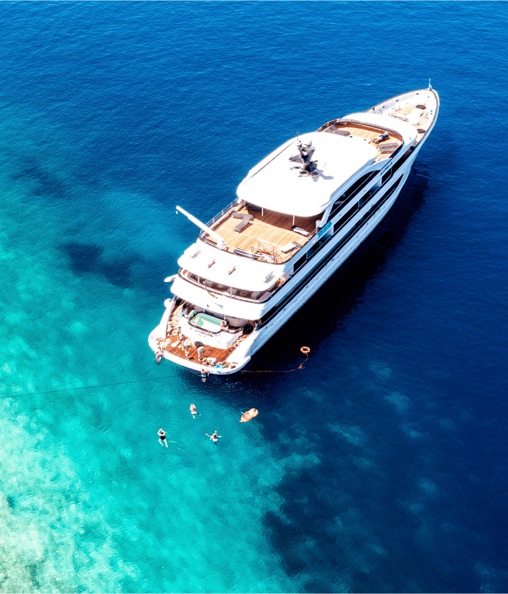 Luxury Yacht Anchored in Turquoise Waters An aerial view of a multi-deck luxury motor yacht anchored in crystal-clear turquoise Mediterranean
