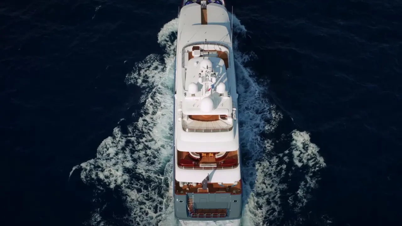 Luxury Yacht Cruising at Full Speed An overhead aerial view of a multi-deck white luxury motor yacht cutting through deep blue ocean