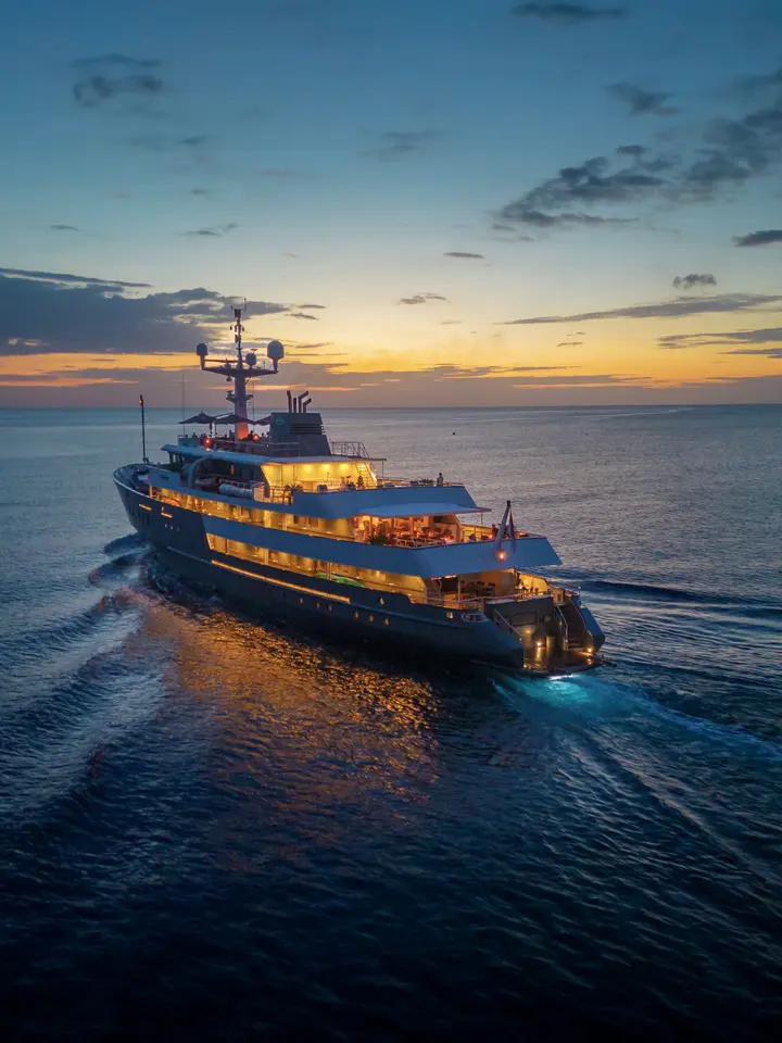 Luxury Yacht at Twilight with Golden Lights A stunning expedition yacht illuminated by warm golden interior lights anchors in calm waters