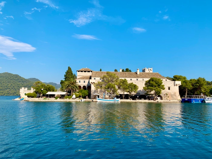 Medieval Fortress on Azure Mediterranean Waters A striking medieval stone fortress situated on a narrow peninsula jutting into crystal-clear turquoise Adriatic waters, surrounded by lush Mediterranean vegetation.