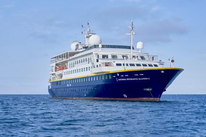 National Geographic Lindblad Cruise Ship at Sea A modern expedition cruise ship with distinctive blue hull and white superstructure sailing on calm blue waters. The vessel features multiple decks, communication equipment on top, and appears to be a luxury expedition cruiser designed for exploration and discovery voyages.