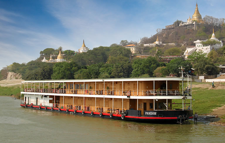 Pandaw River Cruise in Myanmar A multi-deck river cruise boat named Pandaw navigating a river in Myanmar with golden Buddhist
