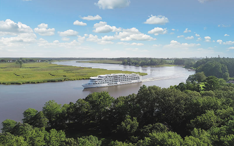 River Cruise Ship Sailing Through Lush Landscape A white river cruise ship navigates through a wide river surrounded by green forests and grassy plains under a blue sky with fluffy white clouds. The landscape appears serene and expansive.