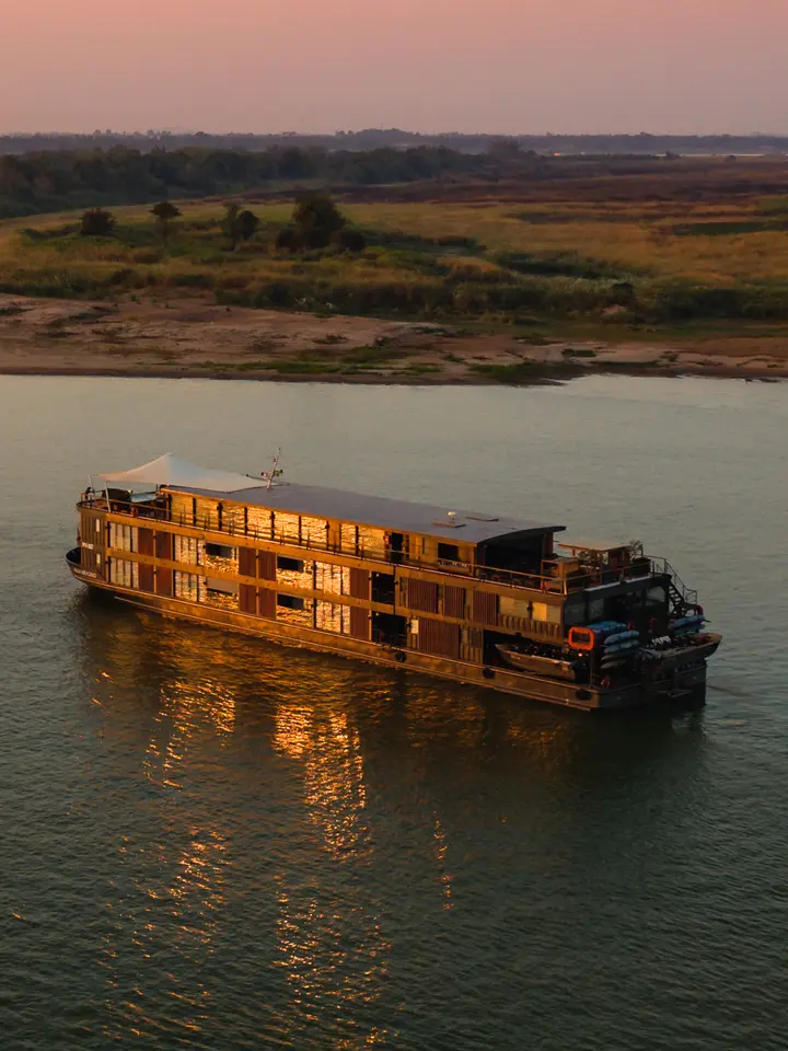 River Cruise Ship at Golden Hour A luxurious river cruise vessel with distinctive golden-lit wooden architecture floats peacefully