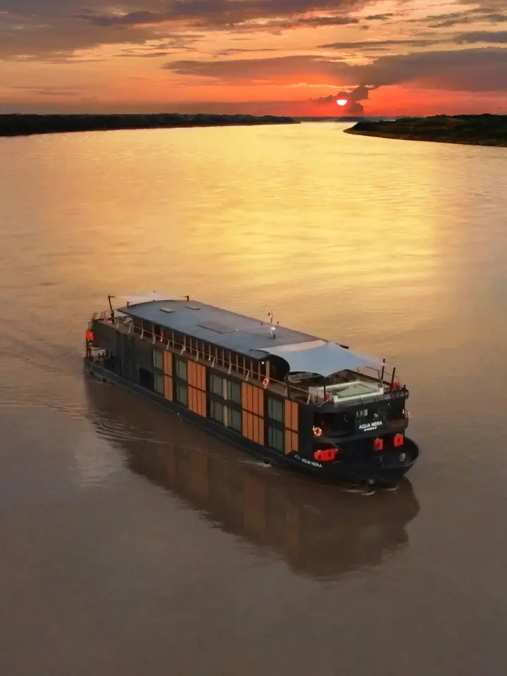 River Cruise Ship at Sunset A modern river cruise vessel with distinctive orange and dark hull coloring navigates a calm, wide