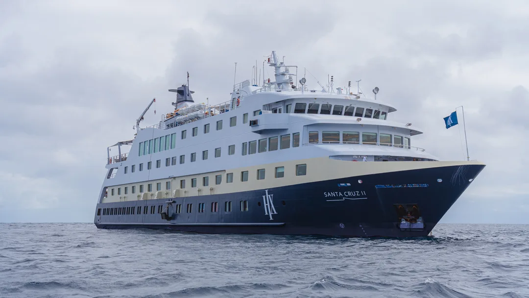 Santa Cruz II Expedition Vessel at Sea A sleek white and navy blue expedition cruise ship sailing on a gray, overcast ocean. The vessel appears to be a small to mid-sized expedition-style ship designed for adventure travel.