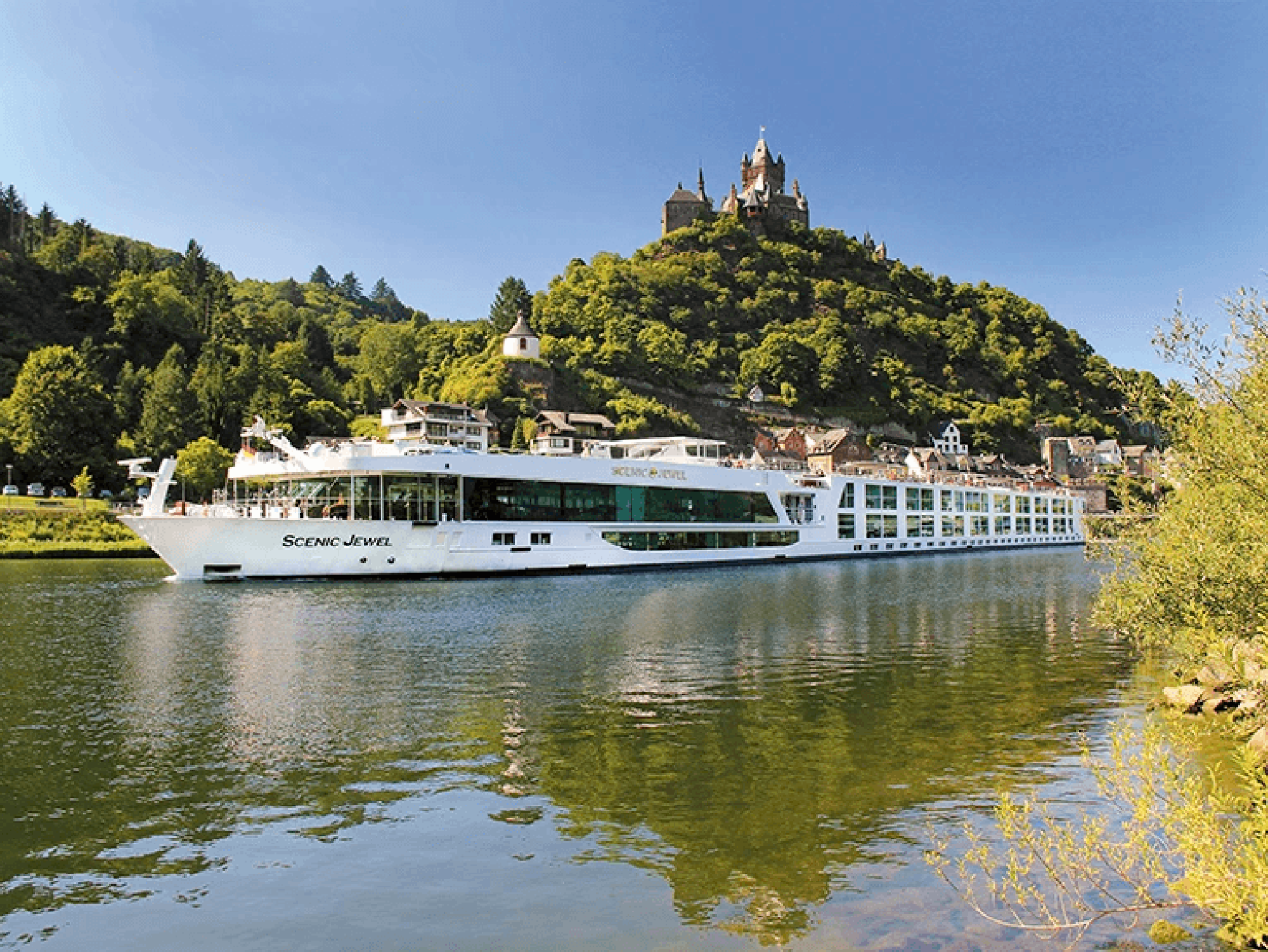 Scenic Jewel River Cruise Past Hilltop Castle A white river cruise ship named Scenic Jewel sailing on a tranquil river with a historic hilltop castle and forested landscape in the background.