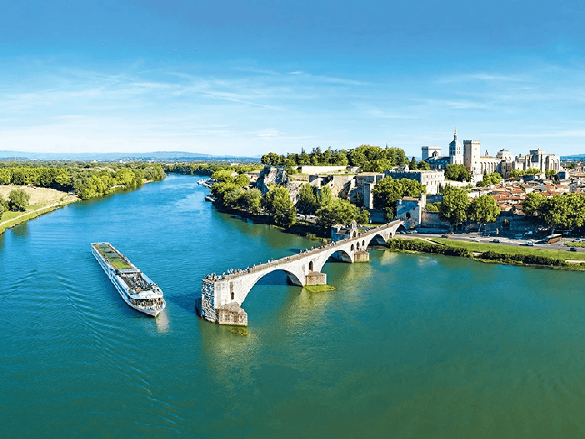 Scenic River Cruise in Avignon, France A river cruise ship passes by the historic Pont Saint-Benezet with the medieval city of Avignon and its famous papal palace in the background.