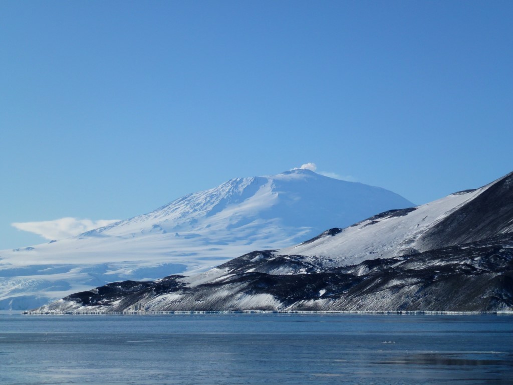 Snow-Capped Volcano Above Frozen Lake A majestic snow-covered volcanic peak rises dramatically above a frozen lake with dark volcanic