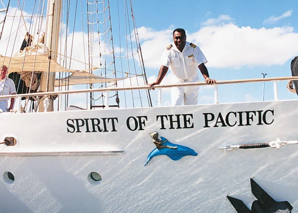 Spirit of the Pacific Tall Ship Crew A crew member in white uniform stands on the deck of the Spirit of the Pacific, a traditional tall