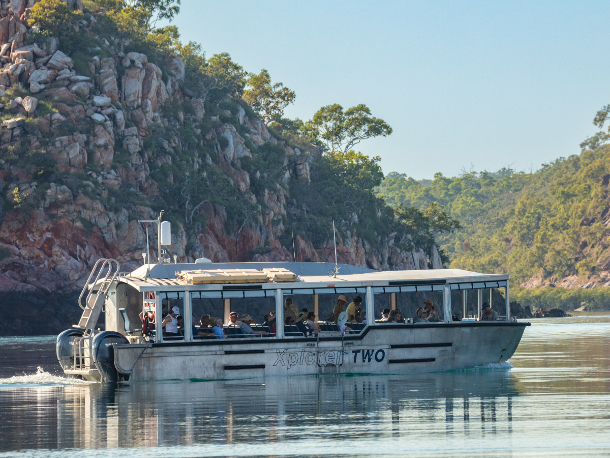Tourist Boat Cruising Rocky Coastline A tour boat named Xplorer Two navigating through a scenic waterway with rocky cliffs and lush vegetation in the background. The boat is filled with passengers enjoying a scenic cruise.