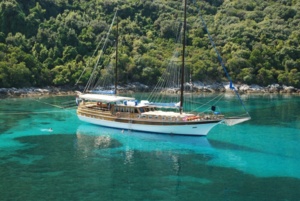 Traditional Gulet Sailing in Turquoise Waters A classic wooden gulet sailing vessel anchors in crystal-clear turquoise waters near a lush