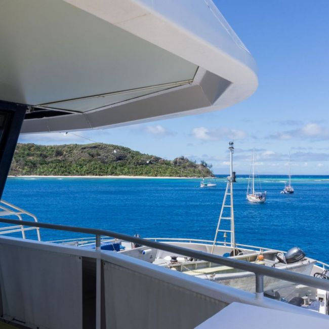 Tropical Island Anchorage with Sailboats A scenic view from a cruise ship's deck showing multiple sailboats anchored in crystal-clear