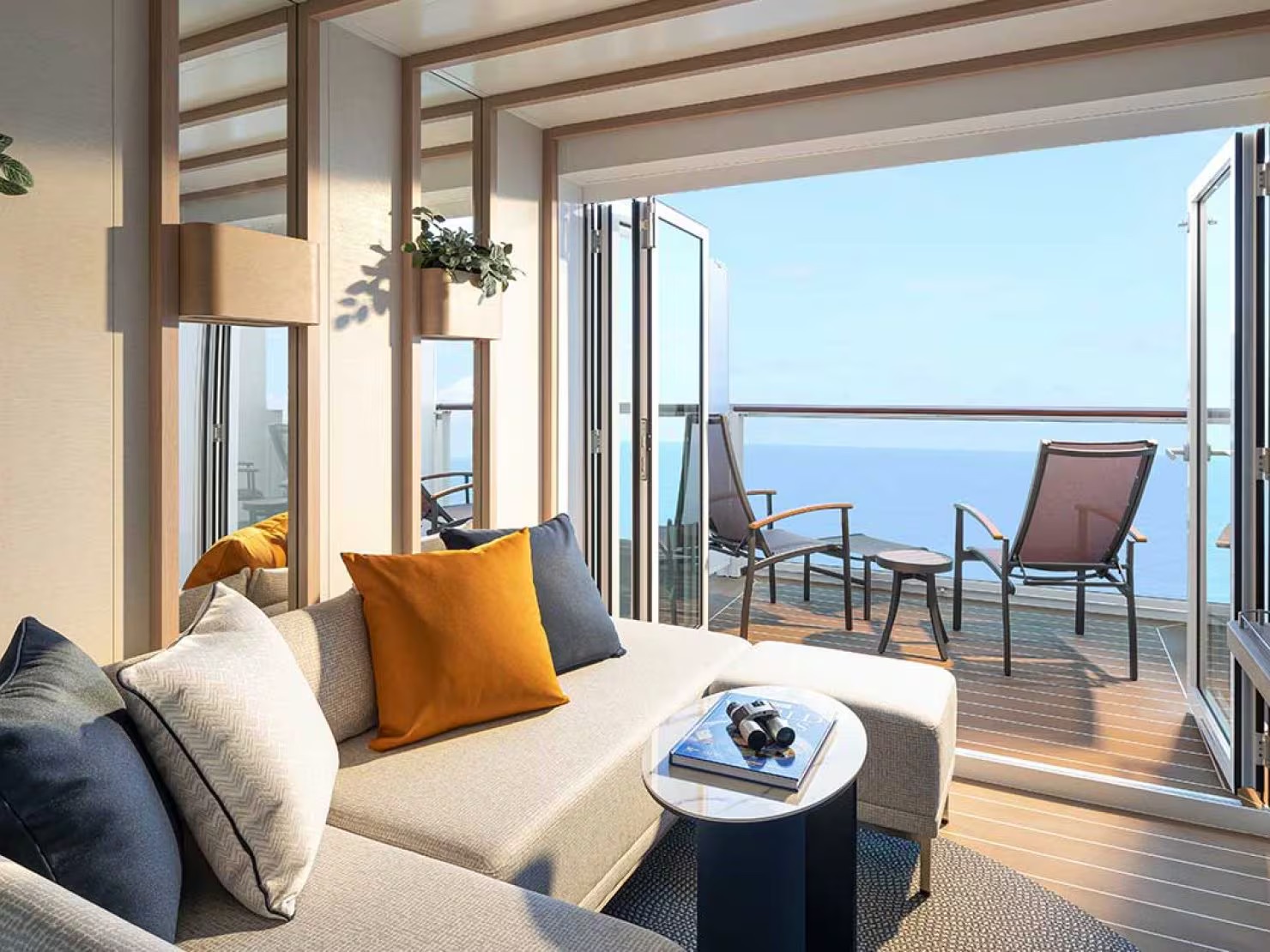 A luxurious modern cabin suite featuring a comfortable sofa with orange and gray pillows, offering expansive ocean views through floor-to-ceiling windows and sliding glass doors that open onto a private balcony with lounge seating.