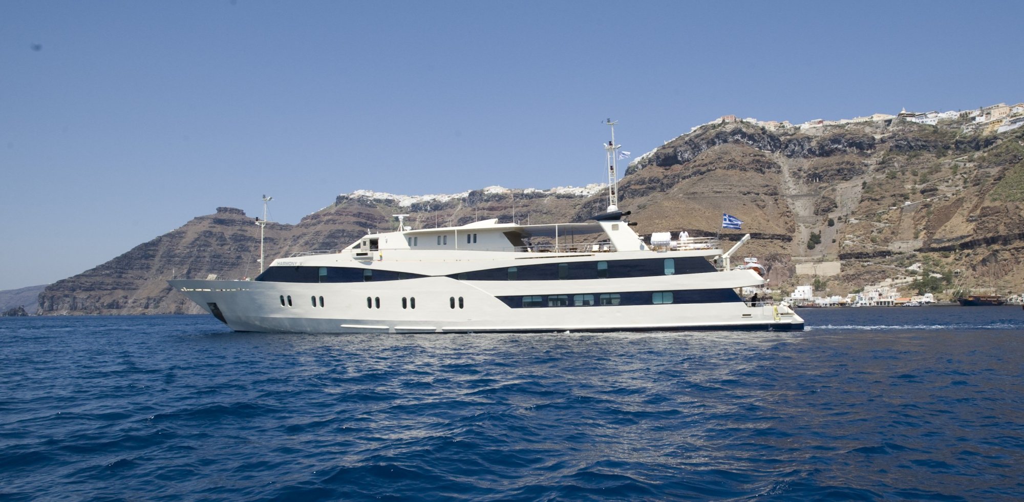 harmony-v-in-santorinui-2bd2a39763 Luxury yacht anchored off Santorini with whitewashed buildings and volcanic cliffs in the background