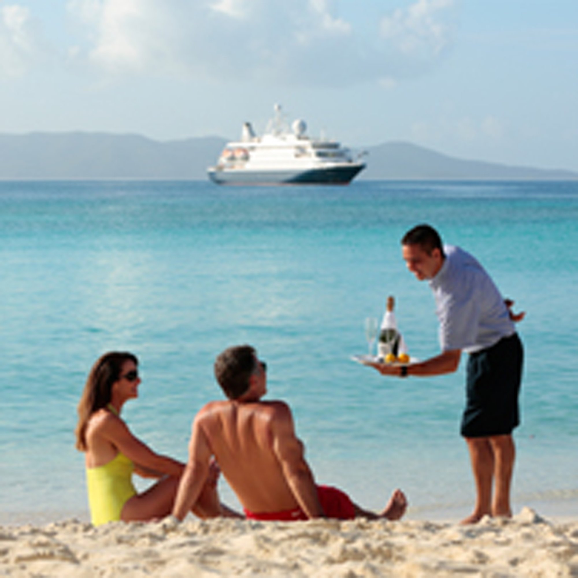 Beach Service from Cruise Ship A waiter serves refreshments to beachgoers on a pristine tropical beach while a large cruise ship anchors in the turquoise waters offshore. The scene captures the luxury and convenience of cruise ship dining with beach service during a port stop.