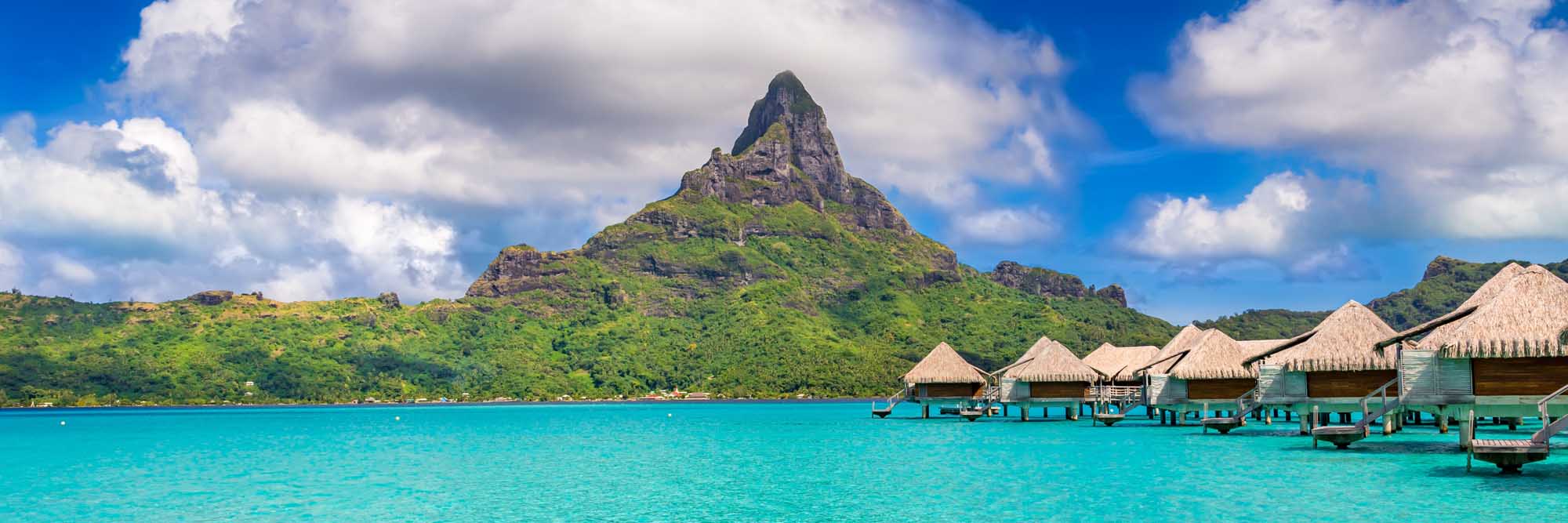 Bora Bora Island with Overwater Bungalows A stunning tropical paradise view of Bora Bora Island in French Polynesia, featuring iconic thatched-roof overwater bungalows in turquoise lagoon waters, with the dramatic volcanic Mount Otemanu peak rising majestically in the background.
