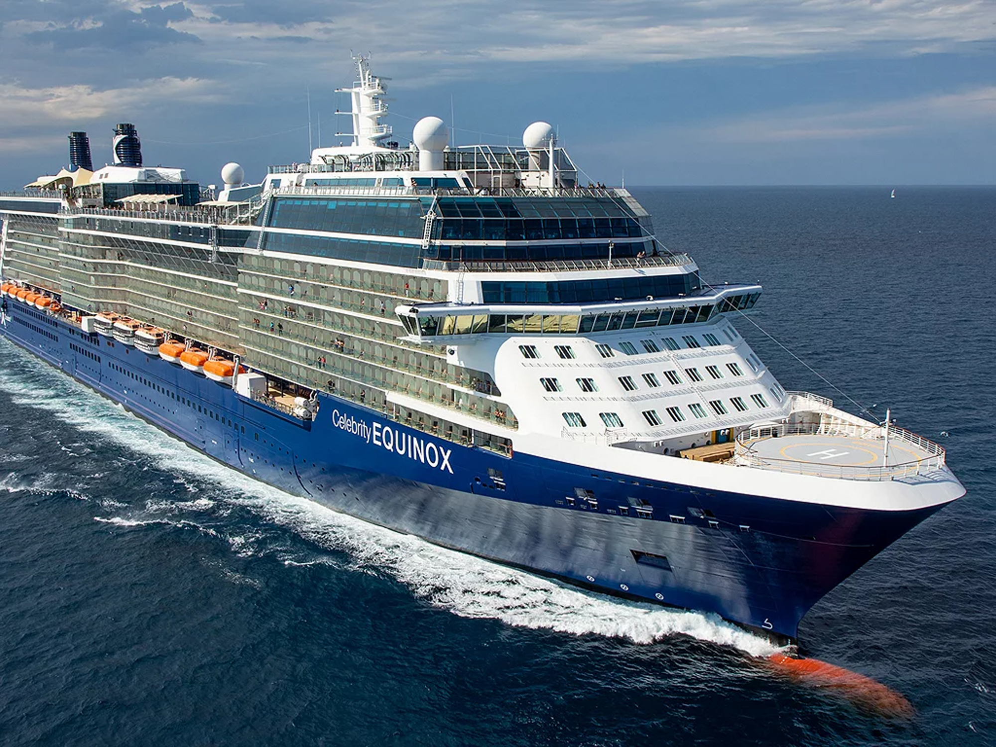 The Celebrity Equinox, a modern luxury cruise ship, sails through open ocean waters under partly cloudy skies. The vessel features the characteristic blue hull and white superstructure of Celebrity Cruises.