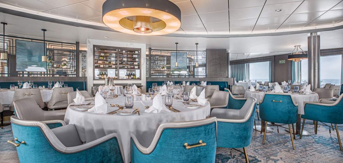 Elegant Fine Dining Restaurant with Turquoise Accents A sophisticated cruise ship dining venue featuring round tables dressed in white linens, modern